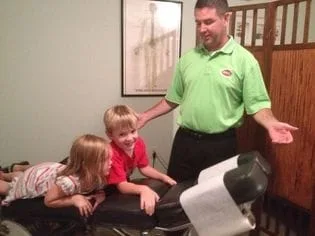Doctor Brown speaking to two children who are laying on an adjustment table