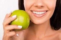 woman smiling white teeth holding apple, Great Neck, NY veneers
