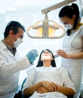 dark haired woman lying back in dental chair, male dentist and female hygienist examining her mouth, tooth extractions North York, ON