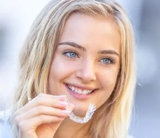 blond teen girl smiling, holding clear teeth aligners, Invisalign Livonia, MI dentist