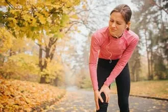 woman holding knee on jogging trail