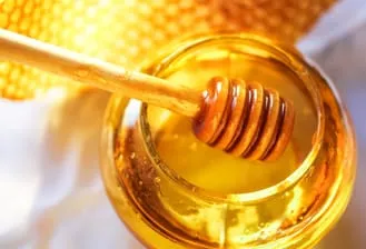An ariel view of a honey dipper entering a jar of honey. The background is white with a honey comb design at the top.