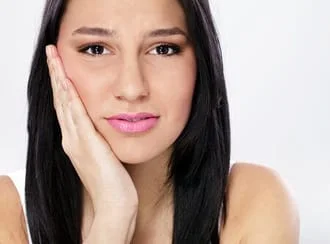 dark haired young woman holding her hand against her jaw, experiencing jaw pain, TMJ Decatur, IL dentist