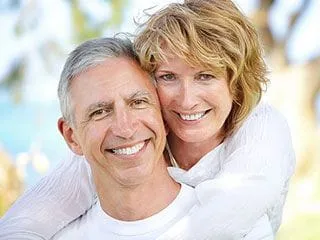 image of older couple hugging and smiling outdoors, trees and water in background, restorative dentistry North York, ON dentist