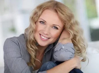 blond woman smiling, sitting with elbow propped on knee and leaning head, dental crowns and bridges Shelby, NC dentist 
