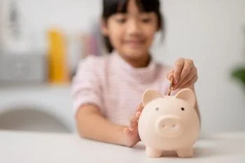 Little Asian girl saving money in a piggy bank from using Oscar Health Insurance Medicare Advantage for chiropractic care