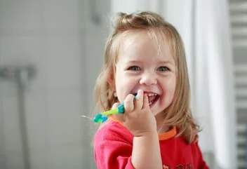 blond toddler girl smiling while brushing teeth, pediatric dentistry Somerville, MA