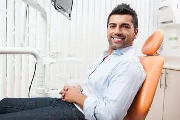 Hispanic man smiling sitting in dentist chair in exam room, dentist Great Neck, NY