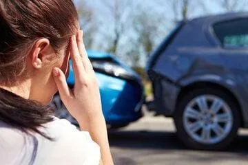 A woman rubs her right temple as she looks at a fender bender