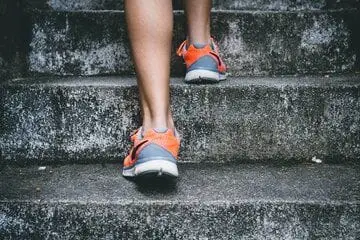 A photo focused on the feet of a person wearing orange and grey shoes while running up a set of stairs.