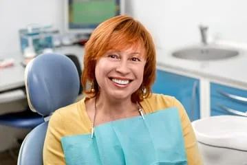older red haired woman smiling sitting in dental exam chair wearing dental bib, CEREC crowns San Diego, CA dentist