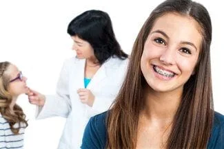 teenage girl smiling with braces, orthodontist in background with other patient. Orthodontics and braces in Northvale, NJ