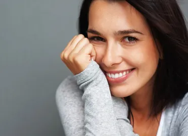 dark haired middle aged woman smiling, leaning face against her right wrist propped up, dental veneers Selmer, TN dentist