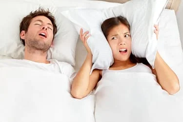 man snoring in bed next to woman covering ears with pillow, can't sleep from loud snoring, sleep apnea Washington, DC