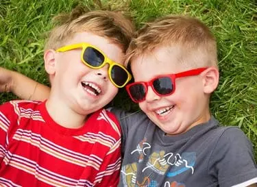 two blond boys with sunglasses laying in grass laughing, pediatric dentistry Brookline, MA