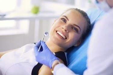 blond teen girl smiling looking up at dentist holding dental tool, dental exam and teeth cleaning Shelby, NC