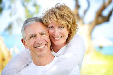 mature couple hugging and smiling outdoors near trees and lake, dental implants Baytown, TX