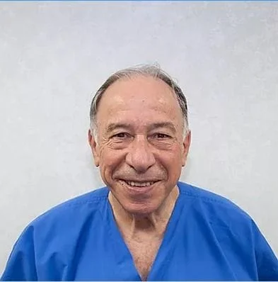 A man in blue scrubs smiling for the camera.