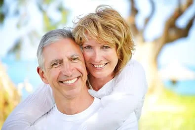 older couple smiling nice white teeth, hugging near beach and trees, dental implants West Hollywood, CA