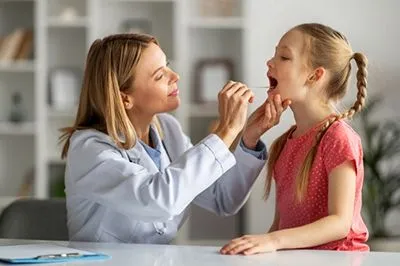 Doctor checking the throat of a young girl in red.