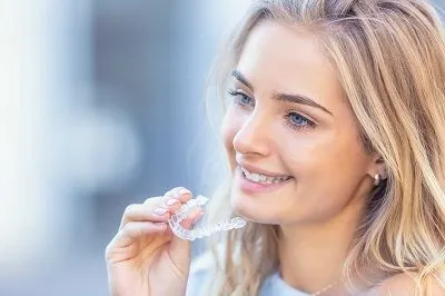 blond teen girl looking left holding clear aligner tray in hand, Invisalign El Cerrito, CA dentist