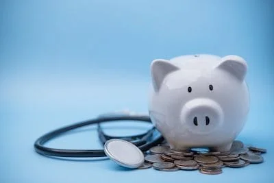 piggybank with coins beside a stethoscope