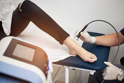 Close-up of laser device applied to ankle for pain relief treatment