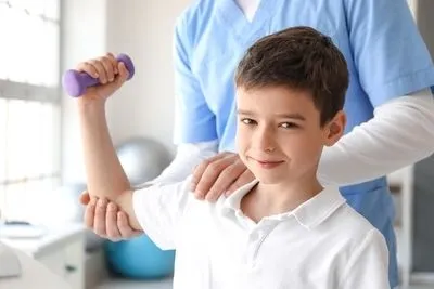 Young boy on clinic with therapist with dumbell.