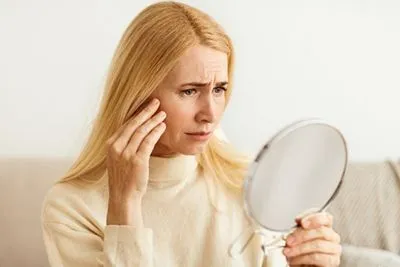 Concerned senior woman examining facial wrinkles in mirror