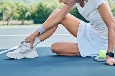 Injured tennis player holding ankle in pain