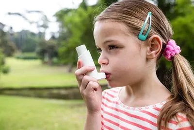 Young girl with asthma using inhaler outside