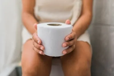 Woman sitting on toilet holding tissue paper due to constipation