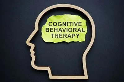 Conceptual illustration of Cognitive Behavioral Therapy written on green paper inside a silhouette of a head.