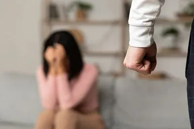 Man's clenched fist with crying woman in the background, symbolizing domestic violence