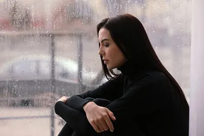 Depressed female sitting quietly by a window on a gloomy, rainy day.