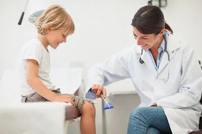 Pediatrician checking child’s knee reflex during physical exam