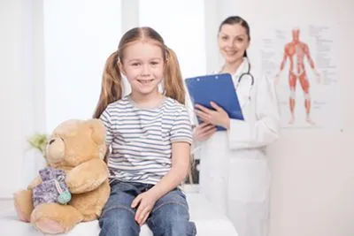 Young girl smiling with toy and doctor on the background