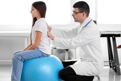 Doctor checking the back of young girl for physical exam