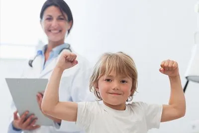 Smiling child flexing muscles after sports checkup with pediatrician