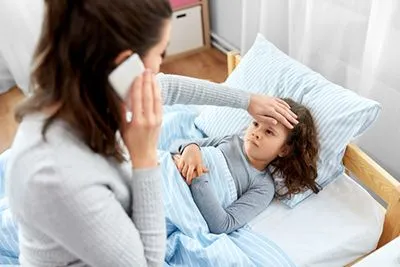 Young girl with fever and mother calling on the phone