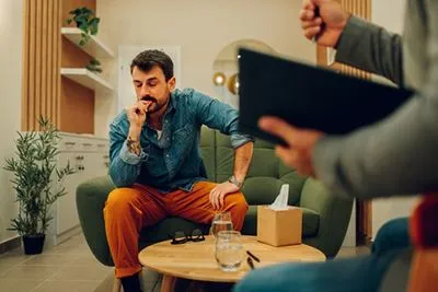 Anxious man biting his nails while talking to a therapist in a counseling session.