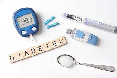 Glucometer and sugar-filled spoon next to wooden blocks spelling 'Diabetes'