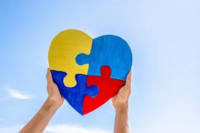 Close-up of hands holding heart-shaped jigsaw puzzle representing autism acceptance