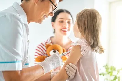 Doctor giving an immunization shot to a young girl with the mother