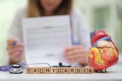 Cardiologist holding heart model with tachycardia word formed by wooden blocks