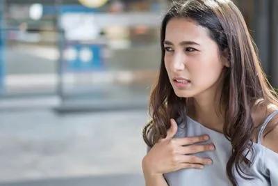 Woman holding chest due to GERD symptoms in outdoor setting