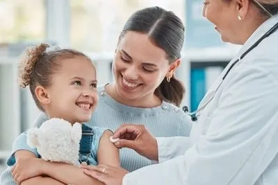 Happy young girl ready for vaccine with mother and doctor in clinic.