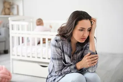 Mother showing signs of postpartum depression with baby in background