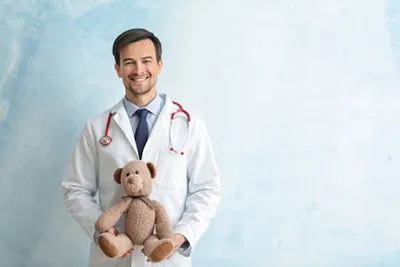 Smiling pediatrician holding a teddy bear against a light blue background