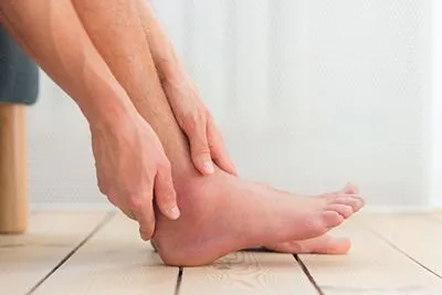 Man sitting while holding his painful, sprained ankle